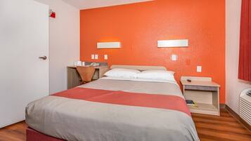 Une chambre d’hôtel avec un lit, des tables de chevet, un bureau et un mur d’accent de couleur rouge-orangée.