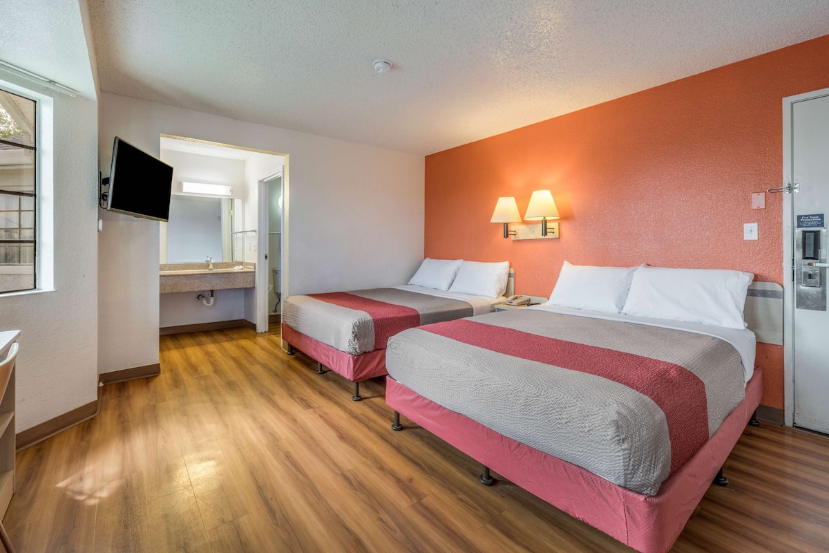 A hotel room with two beds, a TV, a bathroom, and a wooden floor.