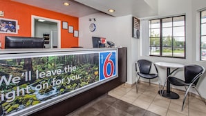 A motel reception area with a large sign, a clock, and two chairs near a window. - Motel 6 Fairfield, CA - North (Fairfield)
