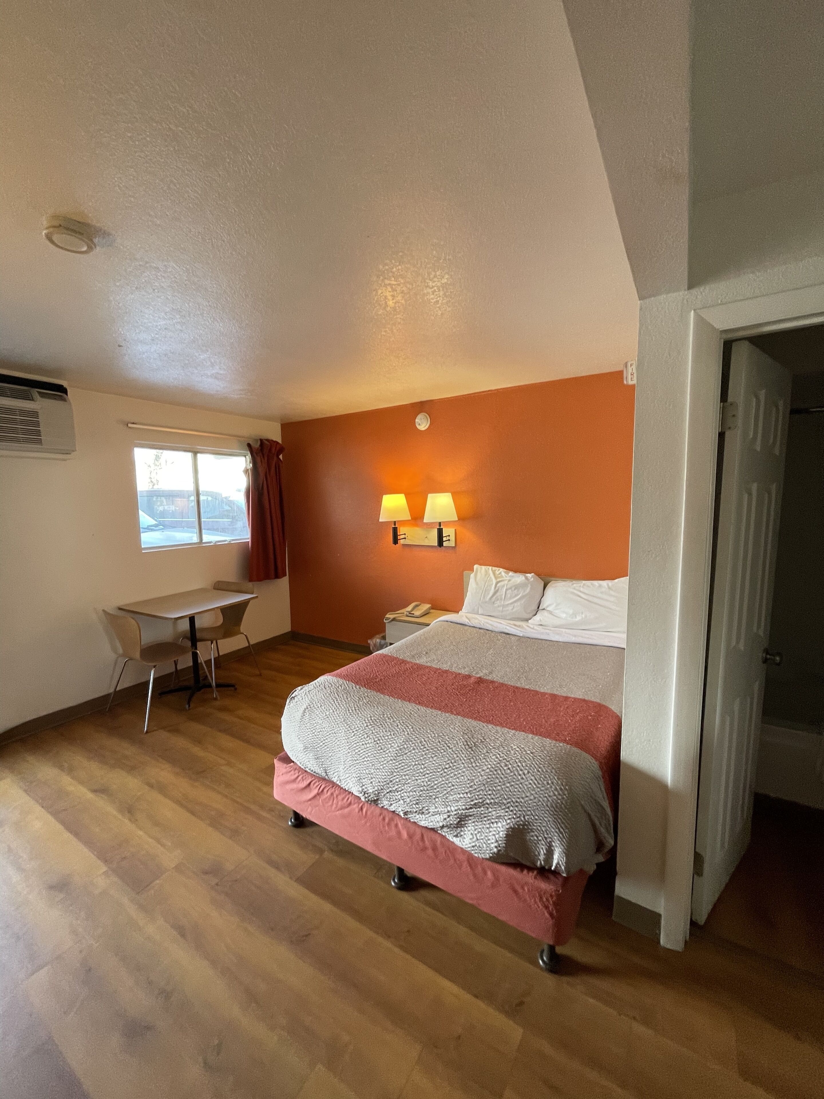 A bedroom with a bed, bedside lamps, a desk, and a window.