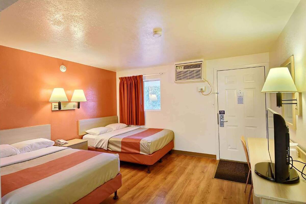A hotel room with two beds, a desk with a computer, a window with curtains, and a door with a sign.