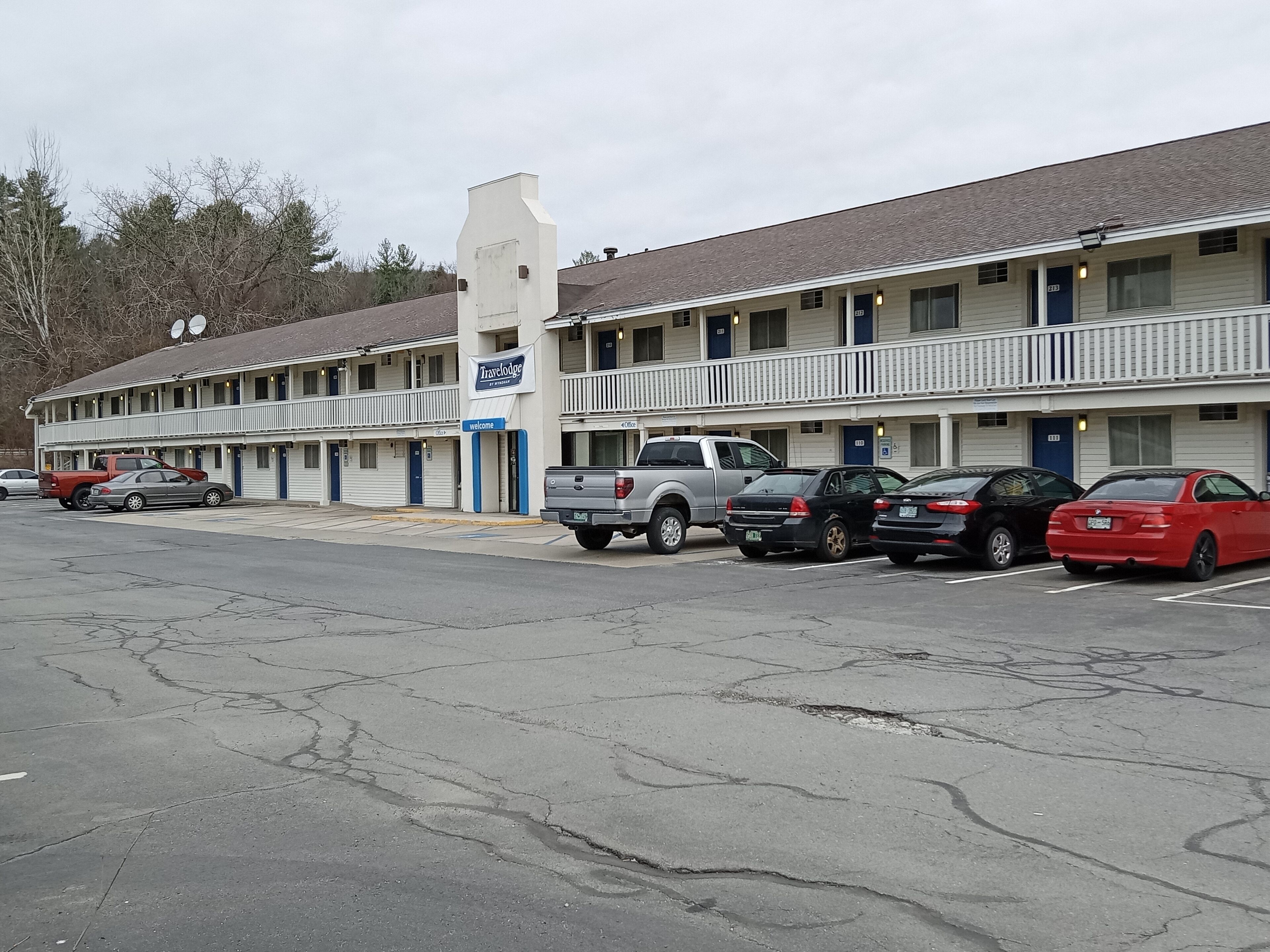 A motel with multiple rooms, a parking lot, and a few vehicles parked in front.