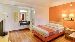 Una habitación de hotel con cama, mesita de noche, lámpara y espejo.