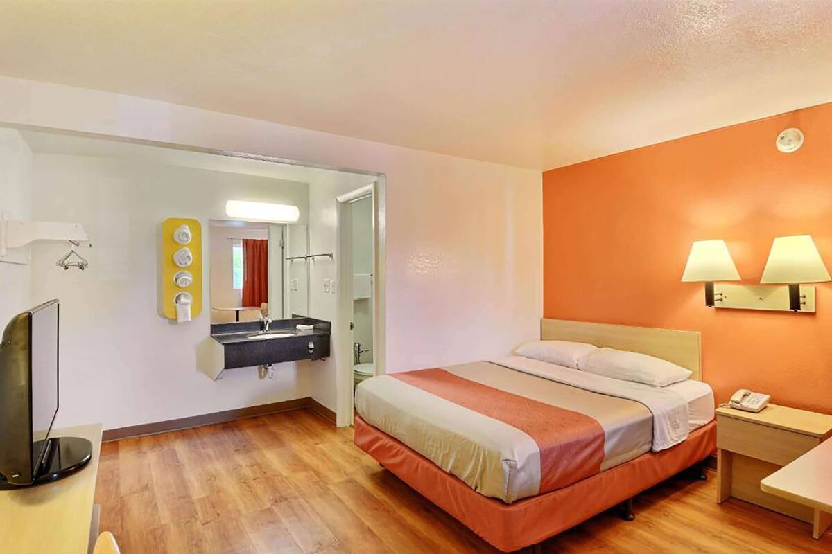 A hotel room with a bed, bedside table, lamp, and a mirror.