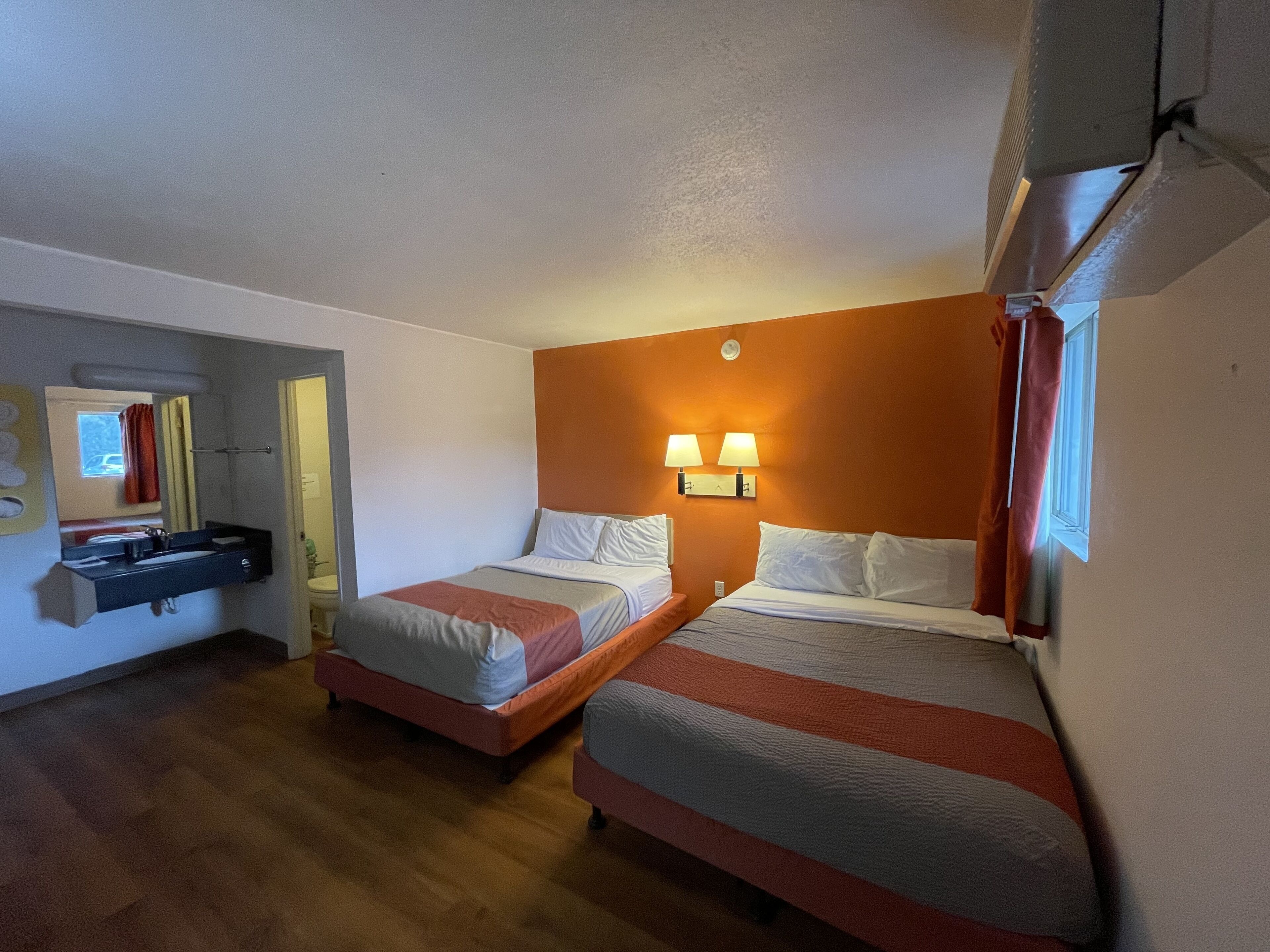 Quarto de hotel com duas camas de solteiro, um banheiro pequeno e um espelho.