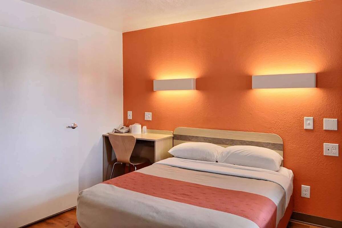 A hotel room with a bed, a desk, and two wall-mounted lights.