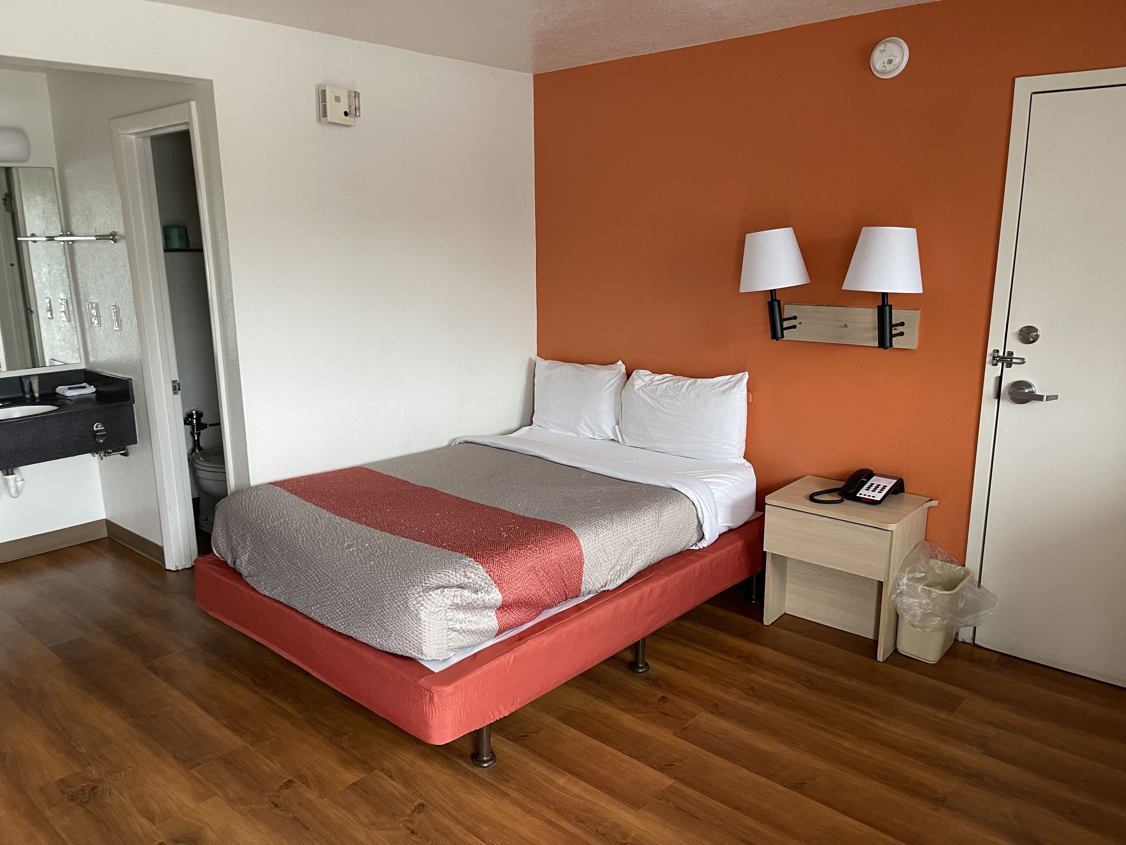 A hotel room with a bed, bedside table, and a bathroom visible through an open door.