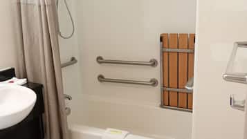 A bathroom with a bathtub, a shower, a handrail, a towel rack, and a sink.