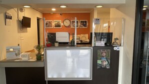Un mostrador de recepción con una computadora, un reloj y un refrigerador.