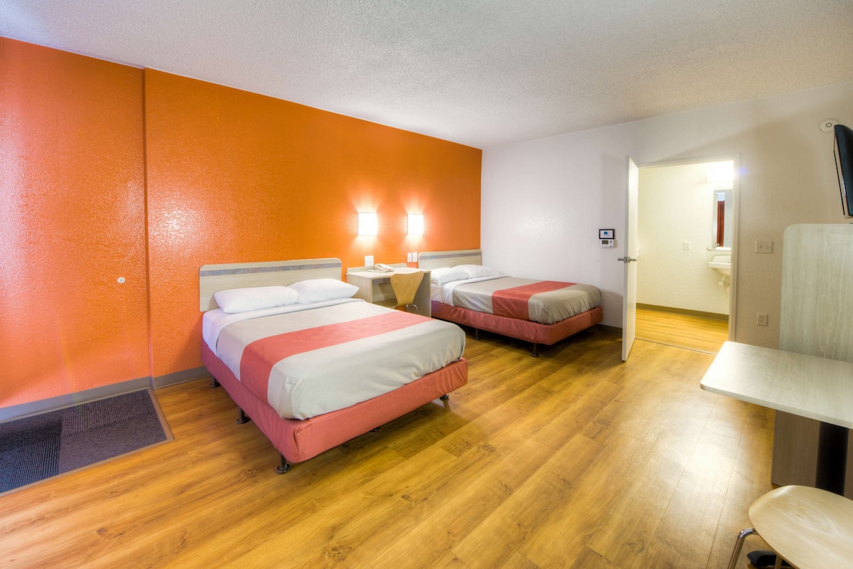 A hotel room with two beds, a wooden floor, and a bathroom visible through an open door.