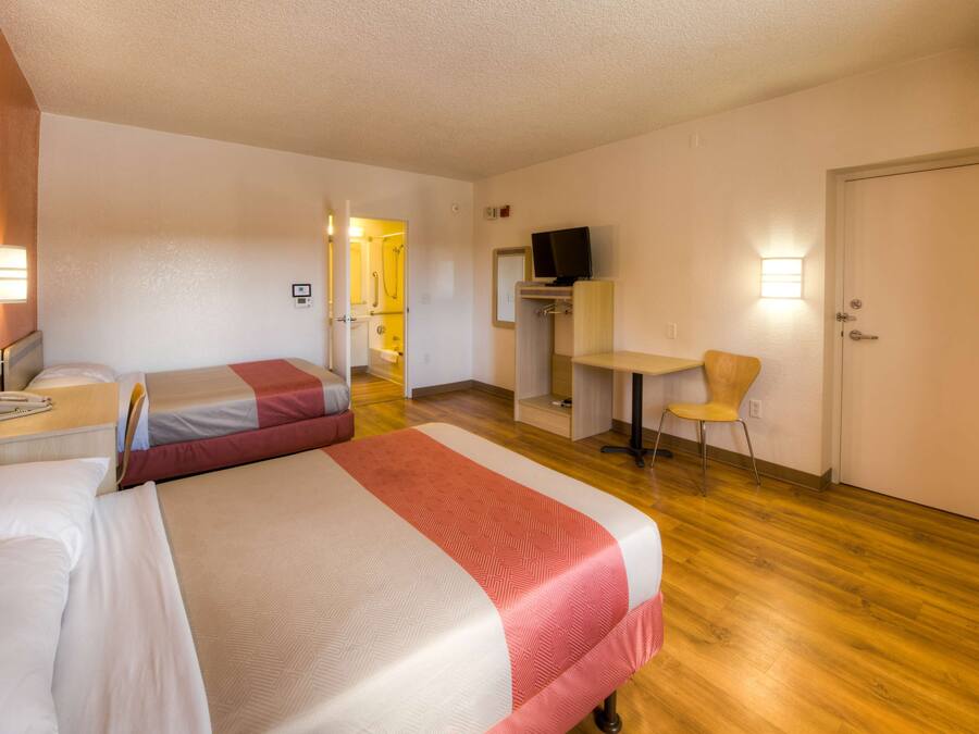 Quarto de hotel com duas camas, uma mesa, uma cadeira, uma televisão e uma porta.