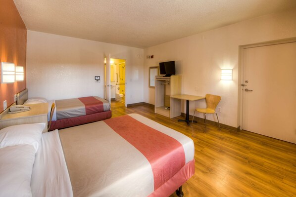 A hotel room with two beds, a desk, a chair, a television, and a door.