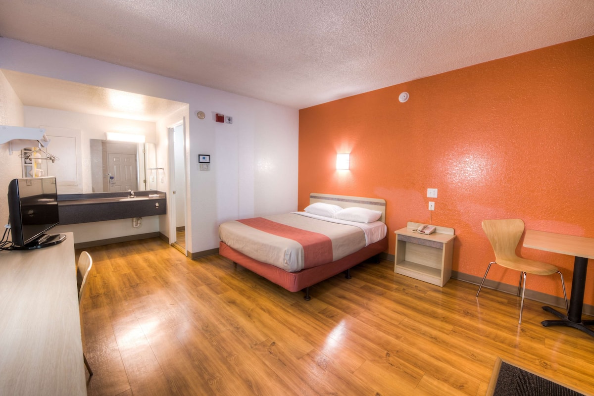 A hotel room with a bed, a desk, a chair, and a small table.