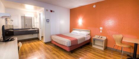 A hotel room with a bed, a desk, a chair, and a small table.