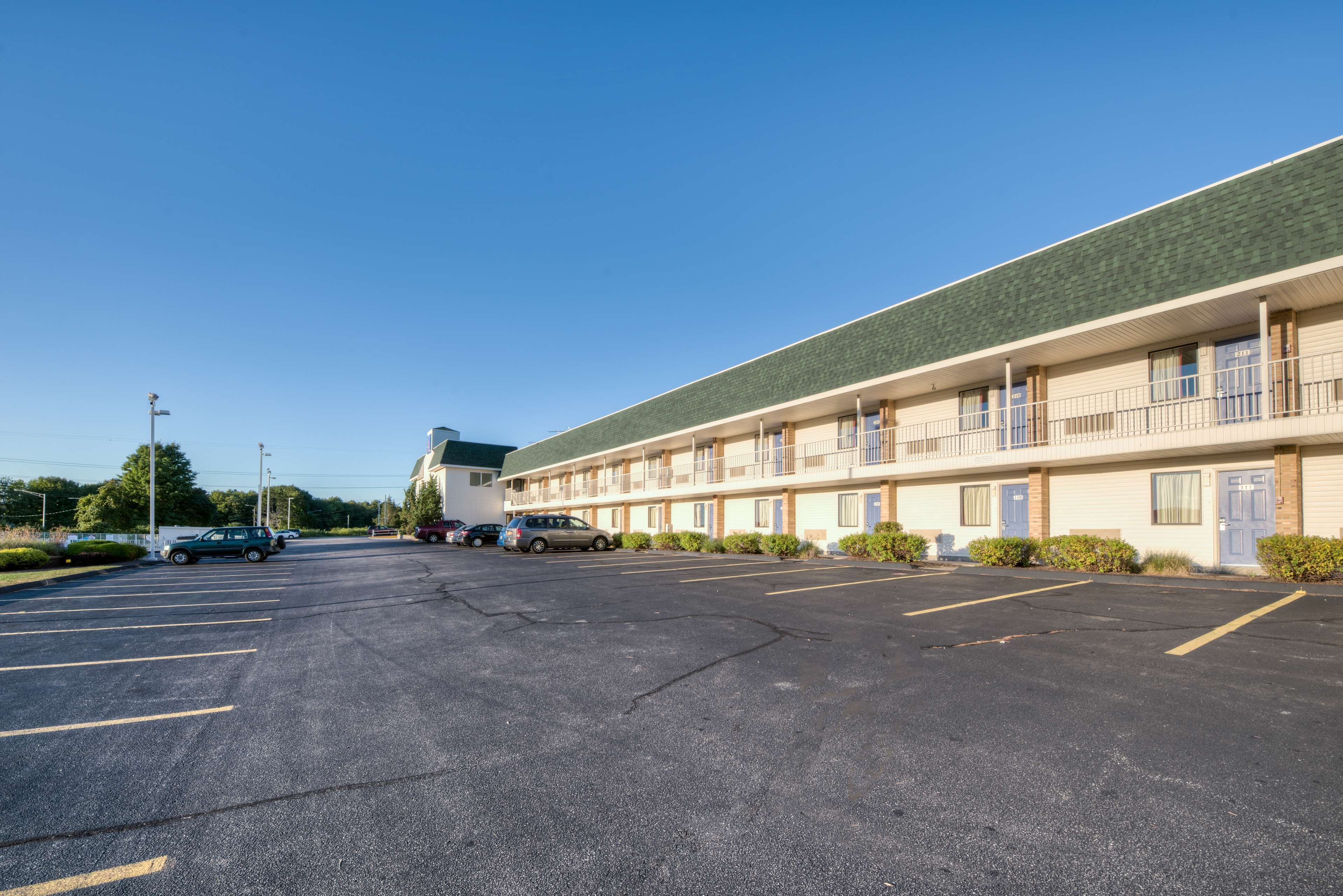 A motel with a parking lot, multiple rooms, and a green roof.