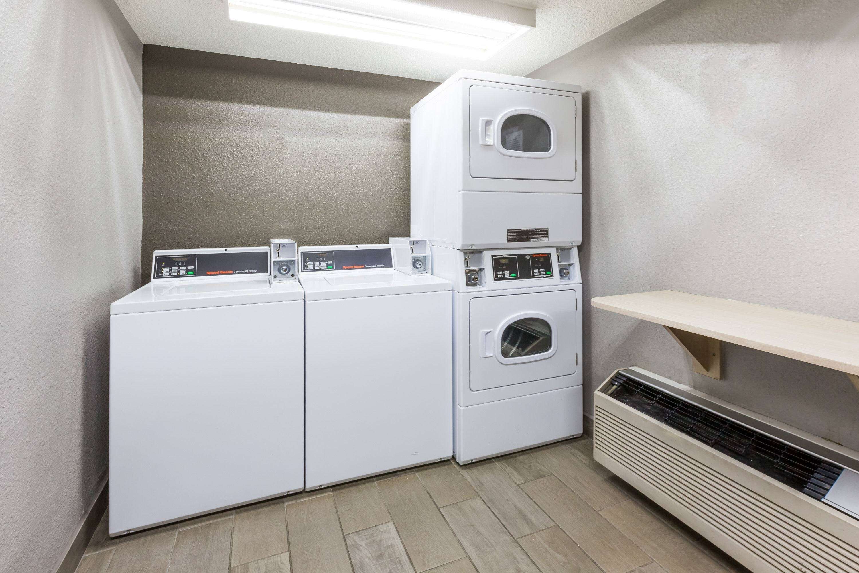 Un lavadero con lavadoras y secadoras apiladas, una unidad de ventilación y un estante.