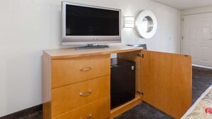 Une pièce comprenant un meuble en bois, un téléviseur à écran plat, un mini-réfrigérateur noir et un luminaire mural rond.