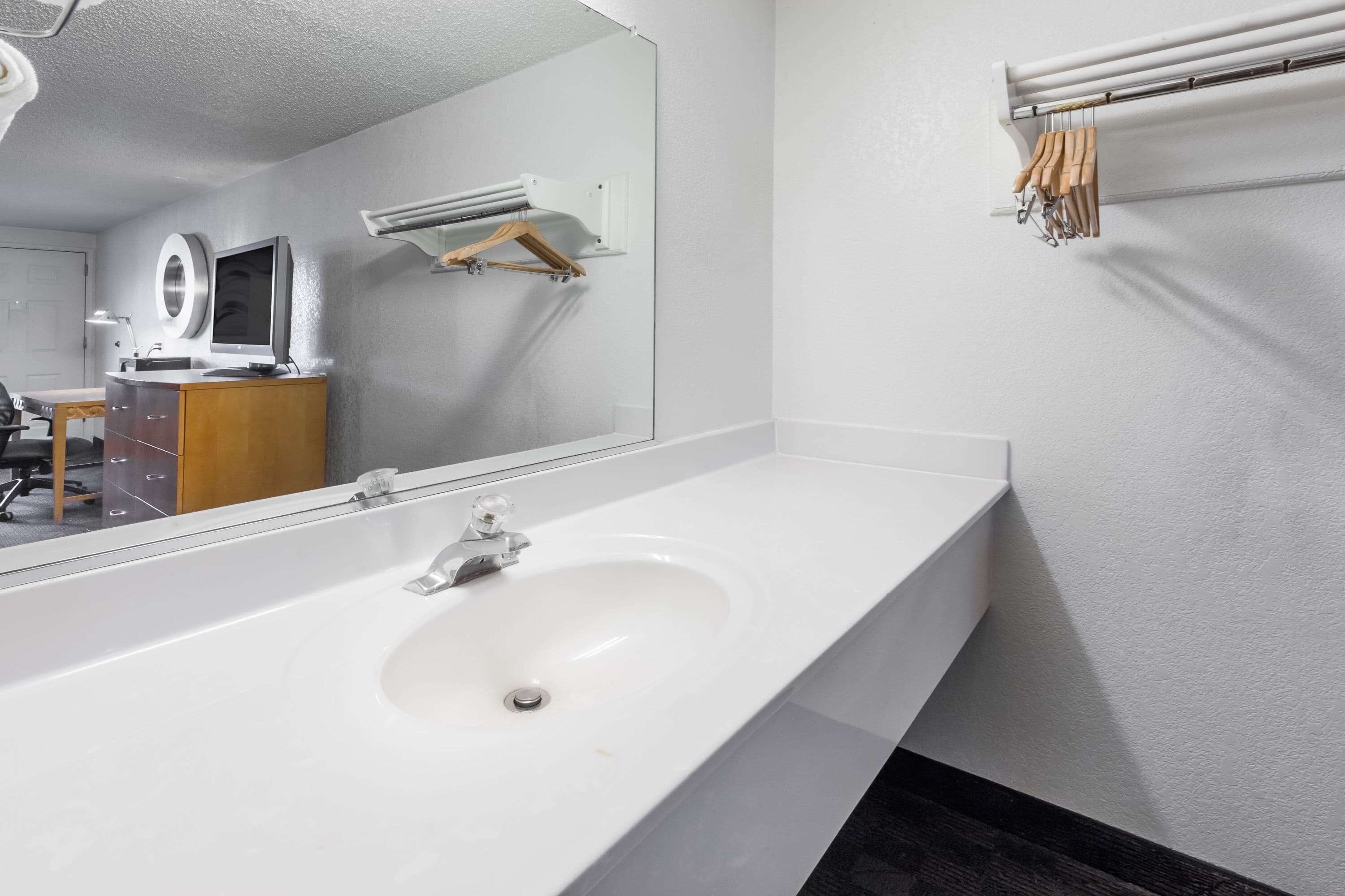 A modern bathroom with a large mirror, a white sink, and a towel rack.