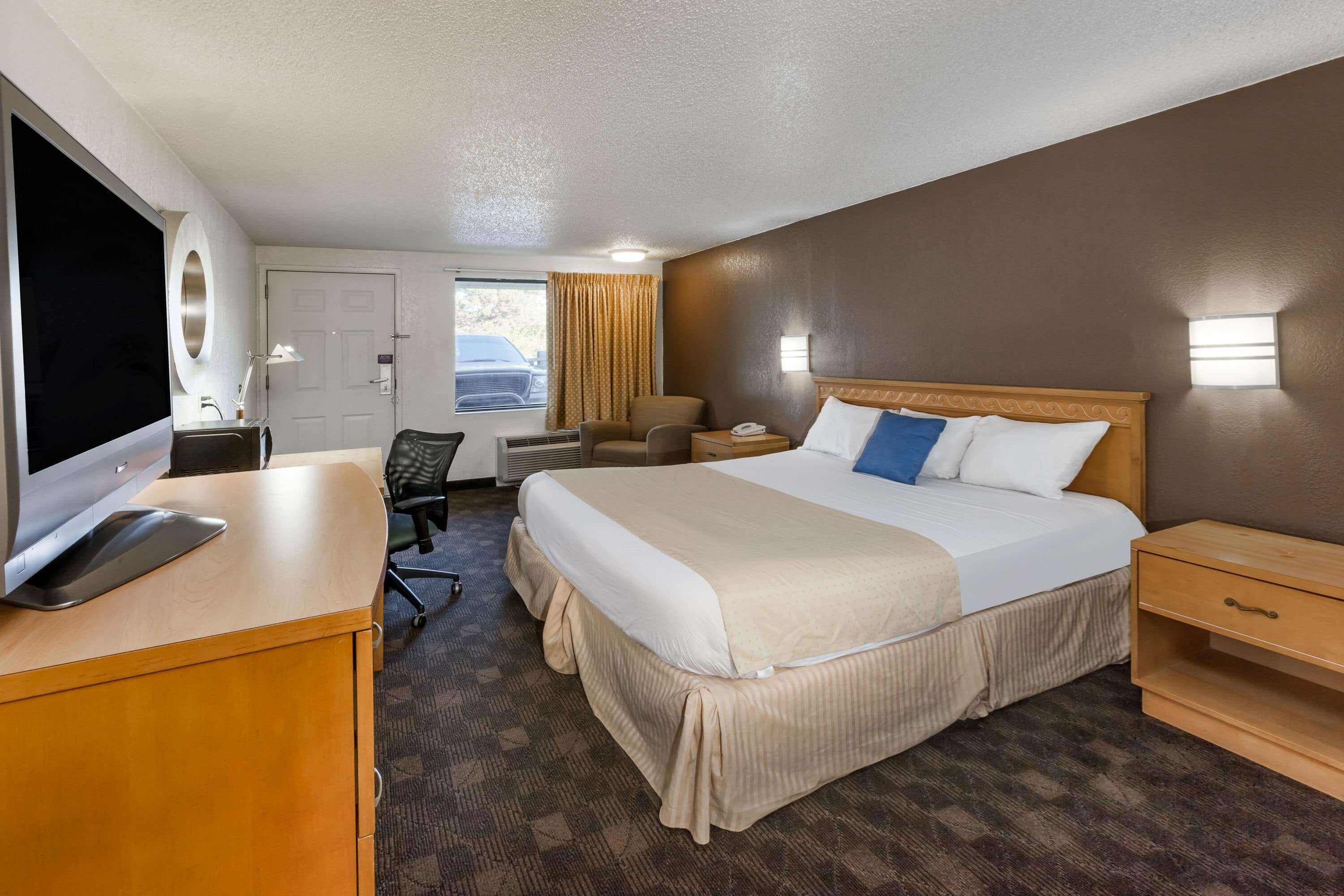 A hotel room with a large bed, a desk with a TV, a chair, a desk lamp, and a window with curtains.