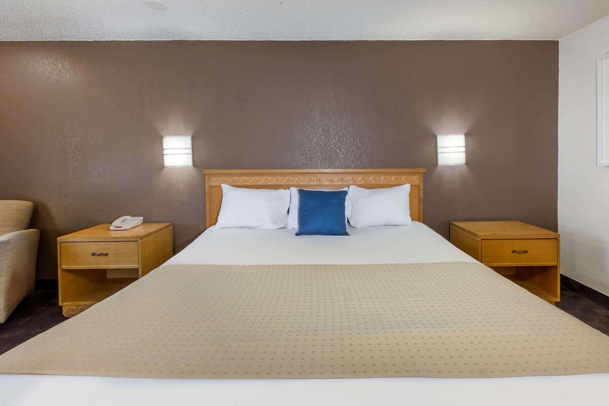 A hotel room with a large bed, two bedside tables, a nightstand, a chair, and two wall-mounted lights.