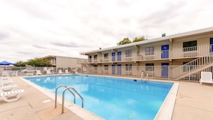 A motel with a swimming pool, multiple rooms, and a covered area with lounge chairs. - Travelodge by Wyndham Norfolk Airport (Norfolk)