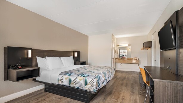 A hotel room with a bed, bedside tables, a desk, a chair, a TV, and a mirror. - Travelodge by Wyndham Norfolk Airport (Norfolk)