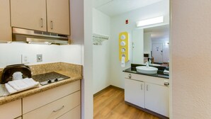 A compact kitchenette with a stove, a small oven, and a toaster. There is a sink with a mirror above it, and a towel rack with towels. - Travelodge by Wyndham Norfolk Airport (Norfolk)