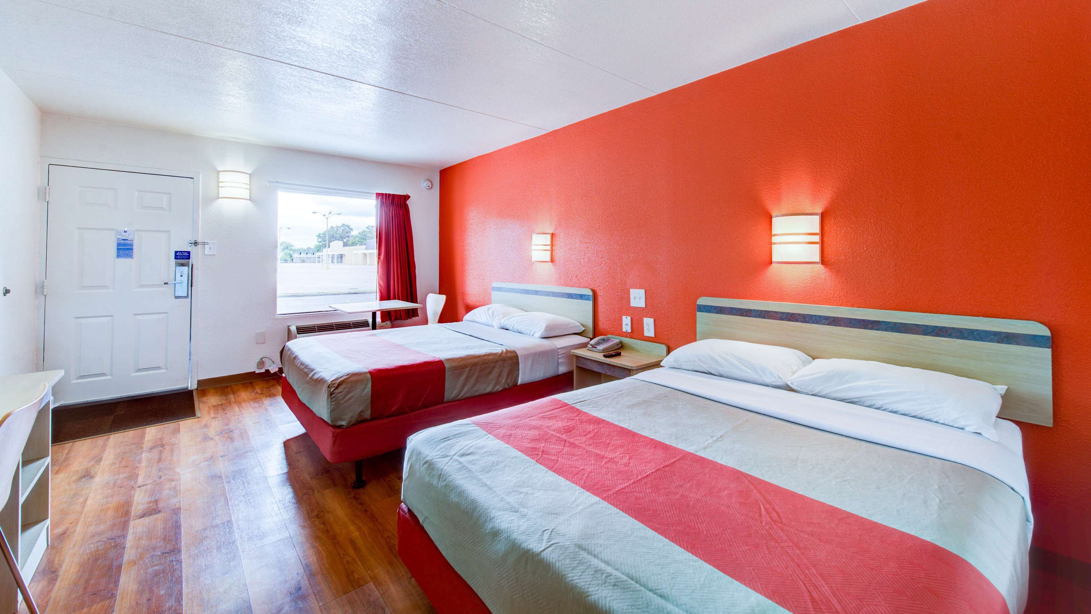 A hotel room with two beds, a window with curtains, a desk, and a door.