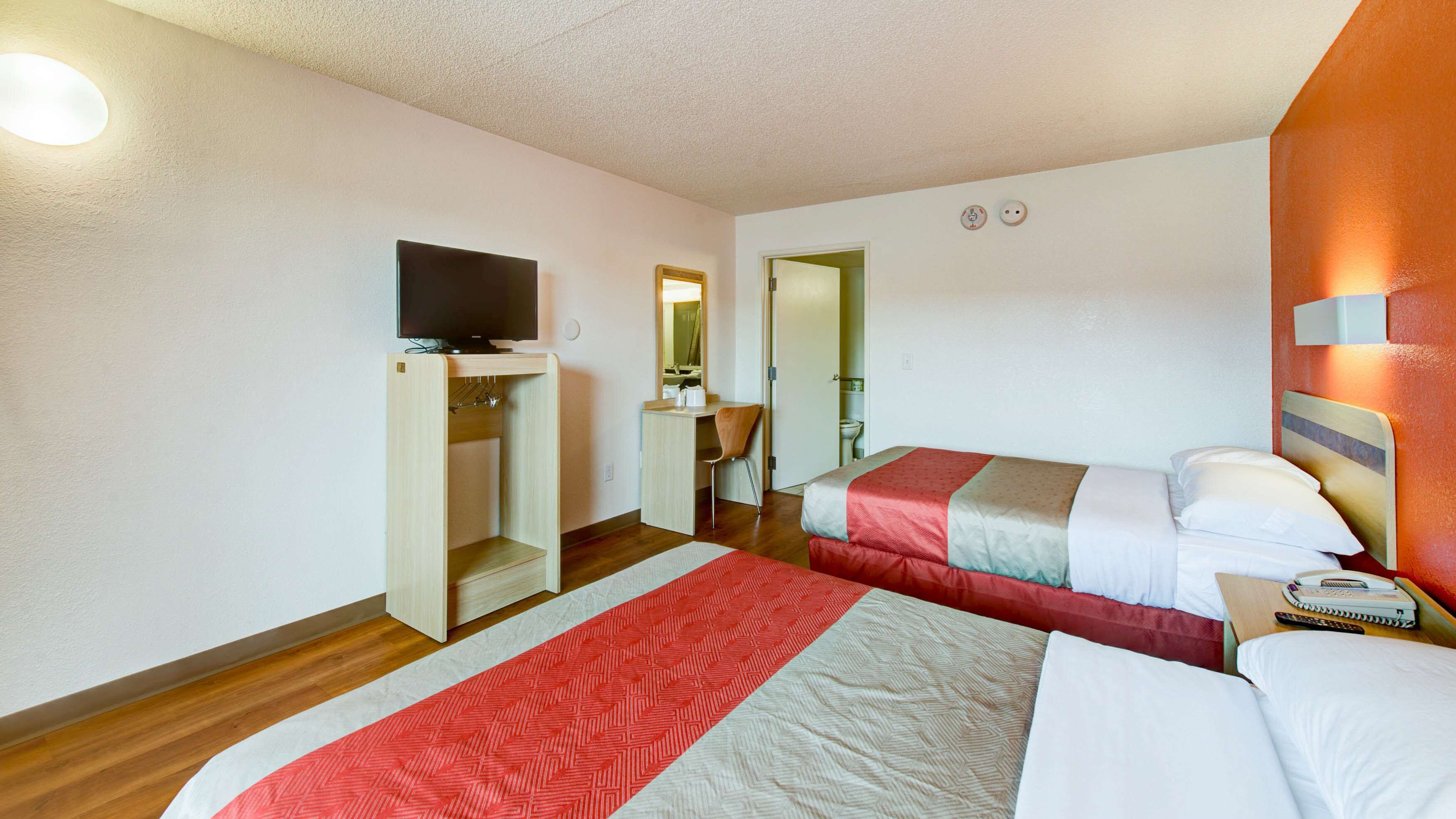 A hotel room with two beds, a TV, a desk, and a mirror.