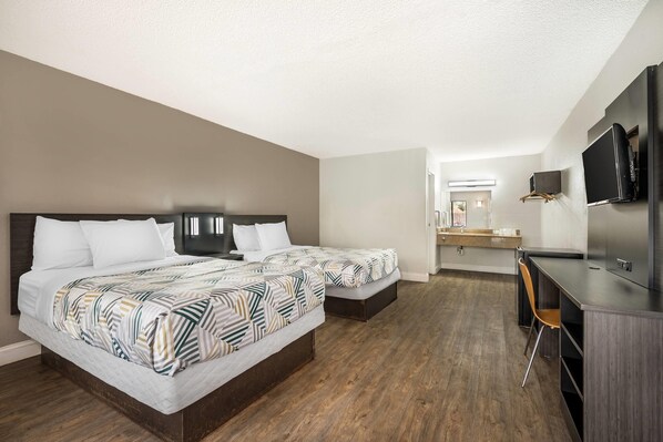 A hotel room with two beds, a desk, a chair, and a TV.
