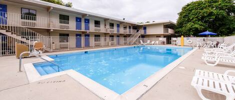 Um motel com piscina, vários quartos e área de deck cercada.