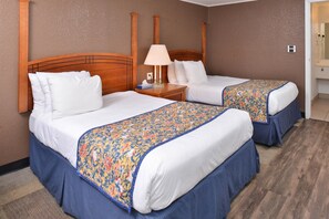 A hotel room with two beds, each with a wooden headboard, a nightstand with a lamp, and a floral bedspread. - Americas Best Value Inn & Suites Jackson, MI (Jackson)