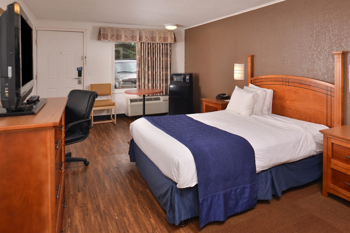 Ein Hotelzimmer mit einem großen Bett, einem Schreibtisch mit Computer, einem Sessel, einem Fernseher und einem Kühlschrank.