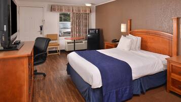 A hotel room with a large bed, a desk with a computer, a chair, a television, and a refrigerator.