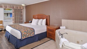 Une chambre d’hôtel comprenant un lit, une table de chevet, une commode, une salle de bain avec baignoire et une fenêtre avec des rideaux.