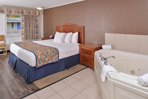 Una habitación de hotel con cama, mesita de noche, cómoda, baño con bañera y ventana con cortinas.