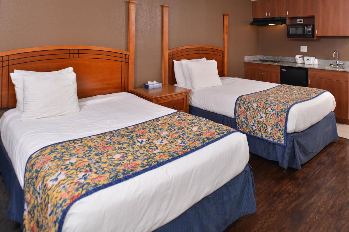 Ein Hotelzimmer mit zwei Betten, einem Holzkopfende, einem kleinen Nachttisch mit Taschentuchbox, einer Mikrowelle und einem Spülbecken in der Küchenzeile.