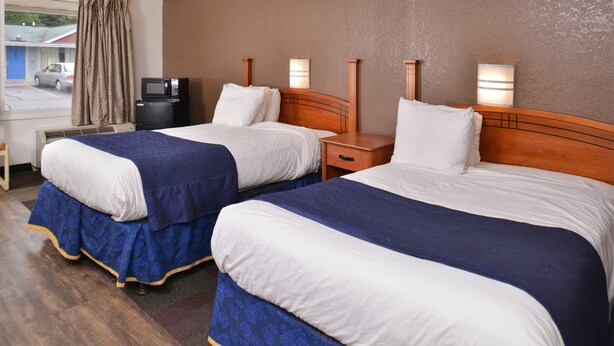 Une chambre d’hôtel avec deux lits, chacun doté d’une tête de lit en bois et de linge de lit blanc. On y trouve des tables de chevet avec des lampes, une télévision et une petite table avec une chaise.