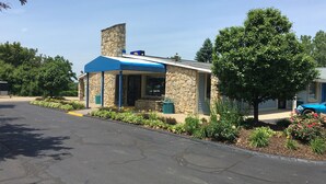 A small building with a stone facade and a blue roof, surrounded by greenery and a paved area. - Americas Best Value Inn & Suites Jackson, MI (Jackson)