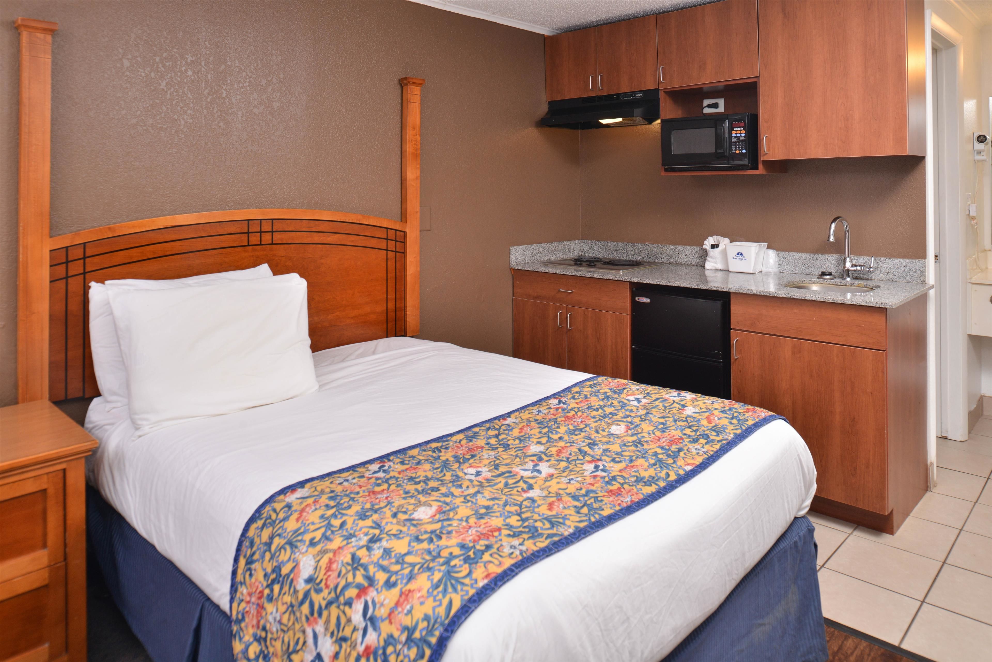 A hotel room with a wooden bed, a small kitchenette with a microwave, and a sink.