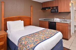 Habitación de hotel con cama de madera, una kitchenette pequeña con microondas y un lavabo.