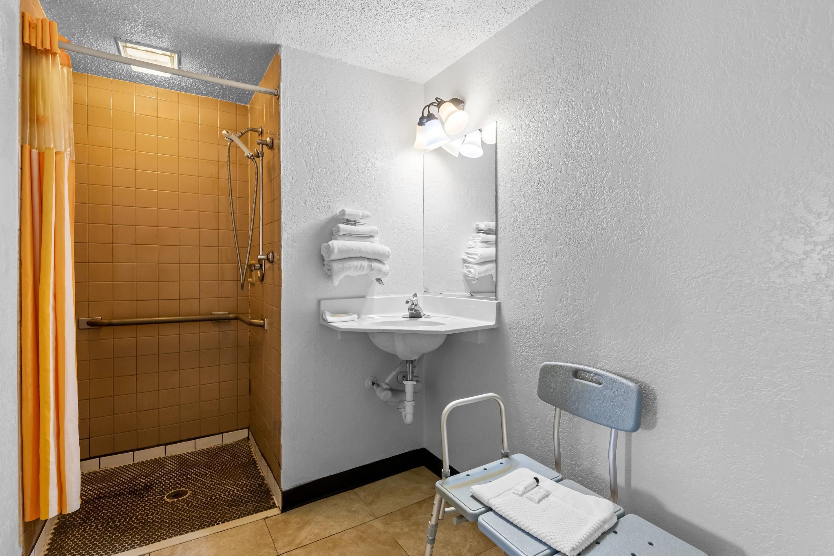 A bathroom with a shower, sink, and a wheelchair-accessible bench.