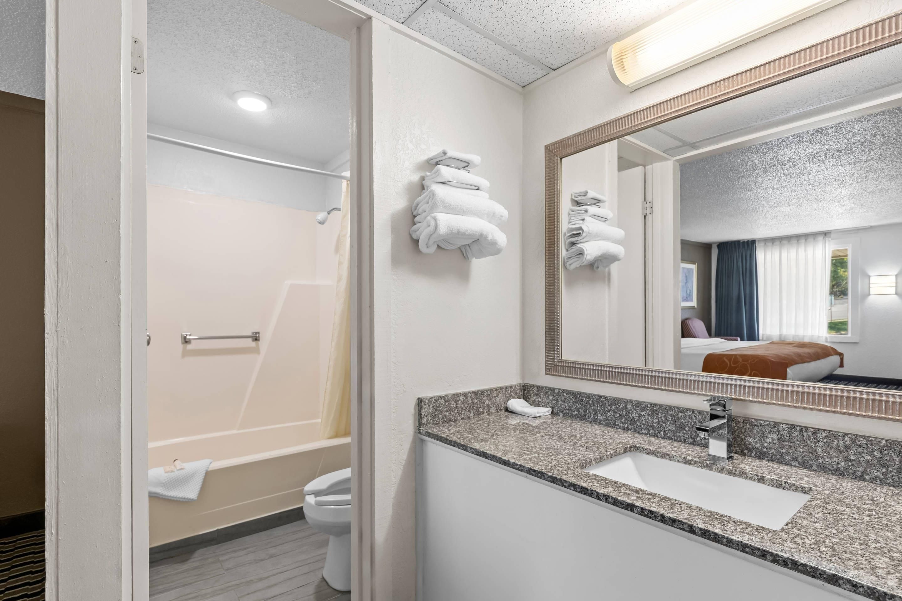A hotel bathroom with a shower, toilet, sink, and a large mirror.