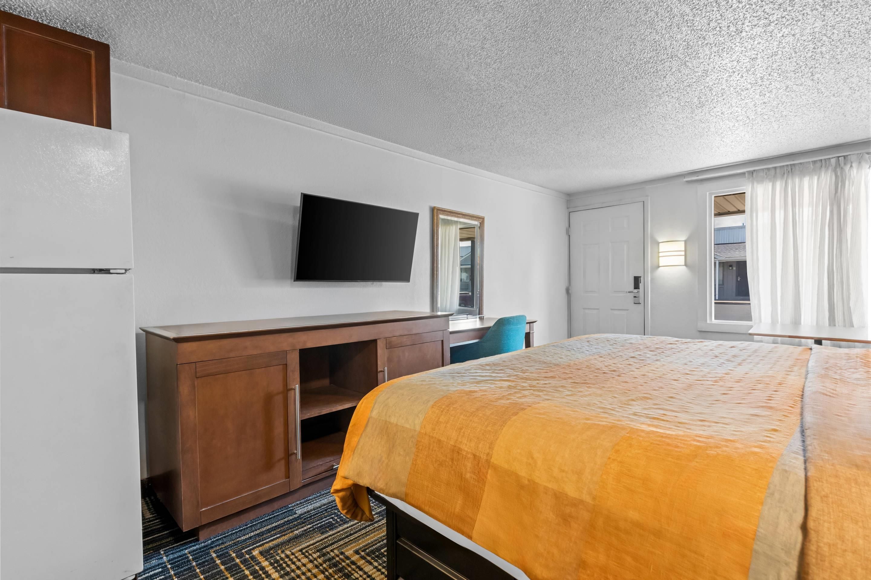 Een hotelkamer met een bed, een aan de muur bevestigde televisie, een bureau met stoel en een kledingkast.
