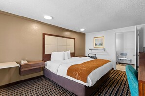 A hotel room with a bed, bedside table, and a desk.