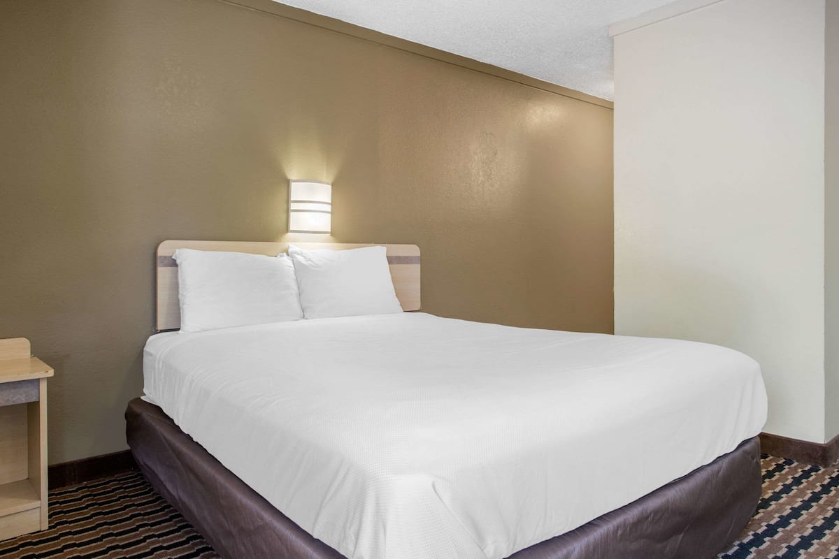 Una habitación de hotel con cama, mesita de noche y una lámpara fijada en la pared.