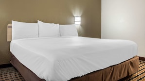Un lit bien fait, avec du linge de lit blanc, dans une chambre d’hôtel aux murs de couleur beige et au tapis à motifs.
