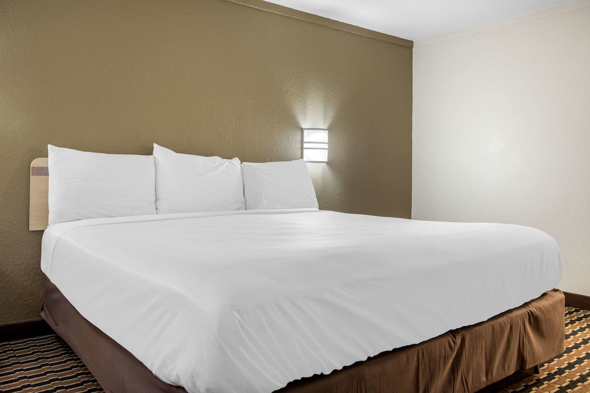 Una cama bien hecha con sábanas blancas en una habitación de hotel con paredes beige y una alfombra estampada.