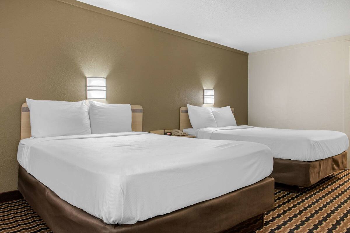 Habitación de hotel con dos camas, cada una con ropa blanca y cabeceras, y lámparas de noche.