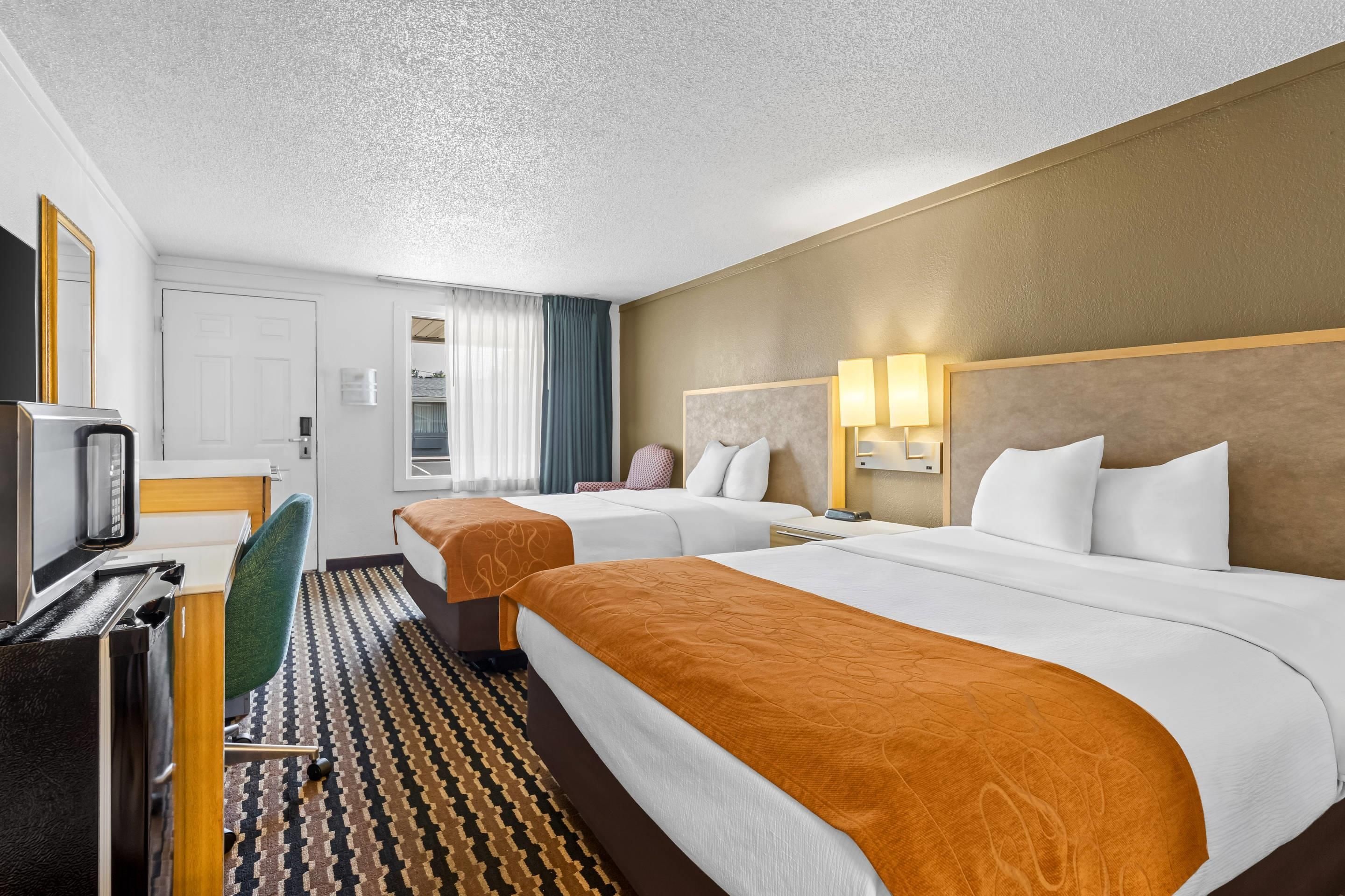 A hotel room with two beds, a desk with a computer, a chair, and a television.
